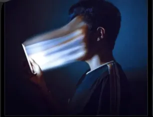A figure whose face dissolves into the light pouring off a phone screen.